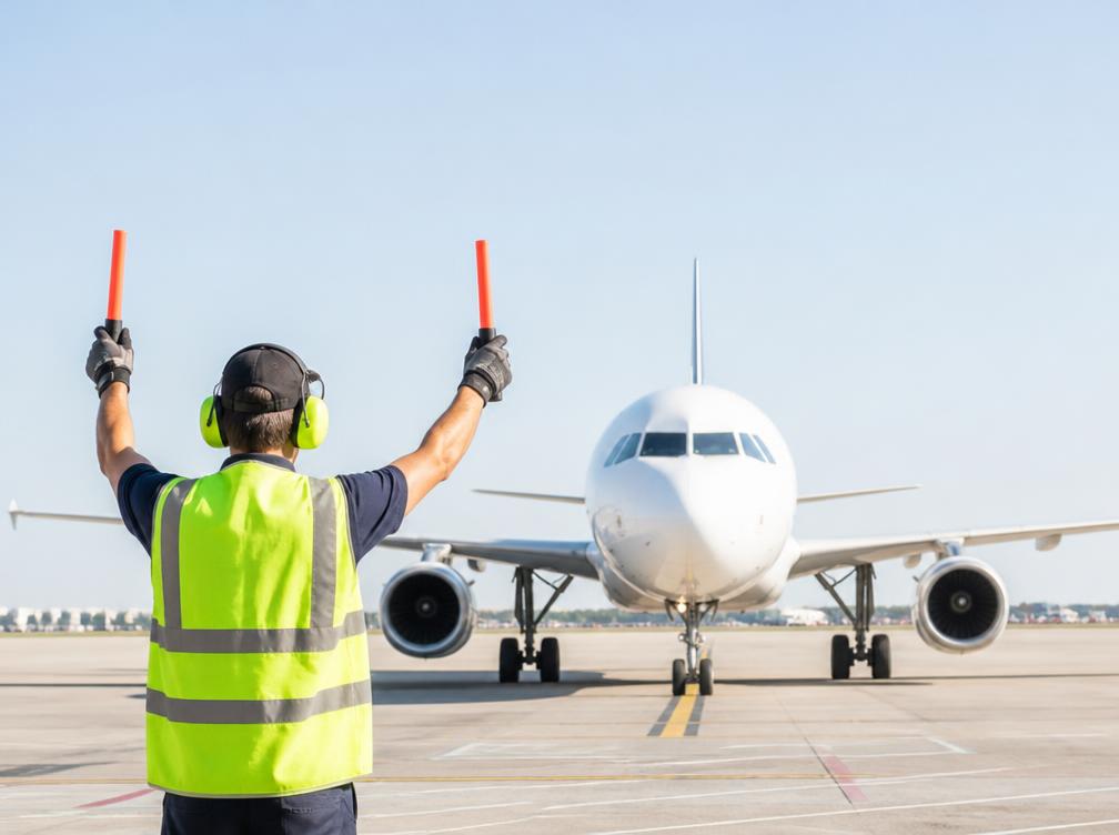 Airport ground crew in a high-visibility vest guiding an aircraft